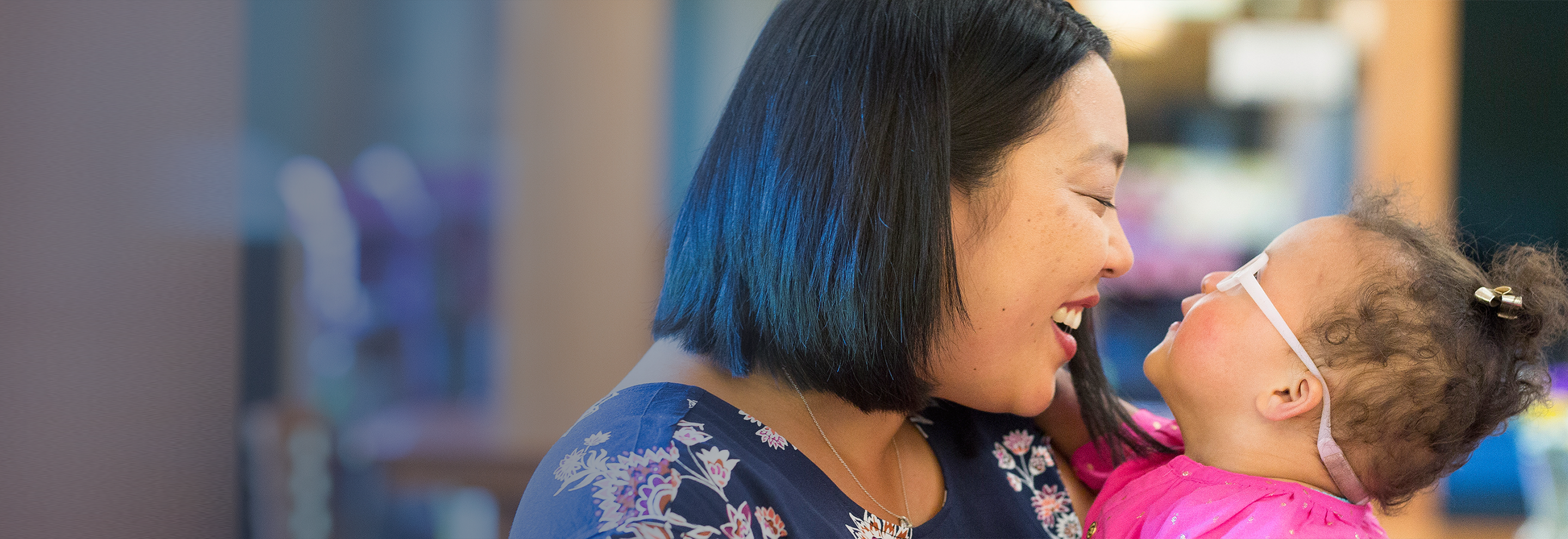 An RMHC family, joyful mother smiling at and holding her infant daughter in glasses