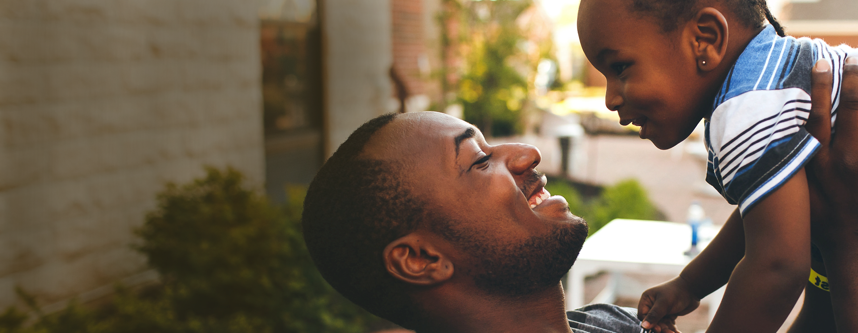 An RMHC family enjoying time outside, a father raising his child in the air as they smile at one another