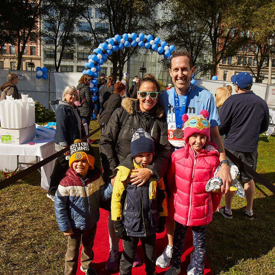 A Run for RMHC marathon dad and family after the finish line, dad in running gear and Run for RMHC shirt, mom and three children in parkas, black, pink, blue and yellow, and red, white, and blue.