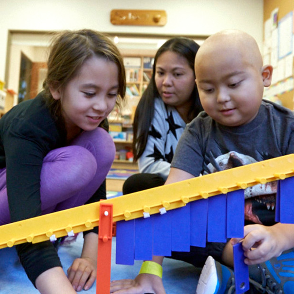 An RMHC family, mom and two children seated and crouching in front of a toy at an RMHC common area