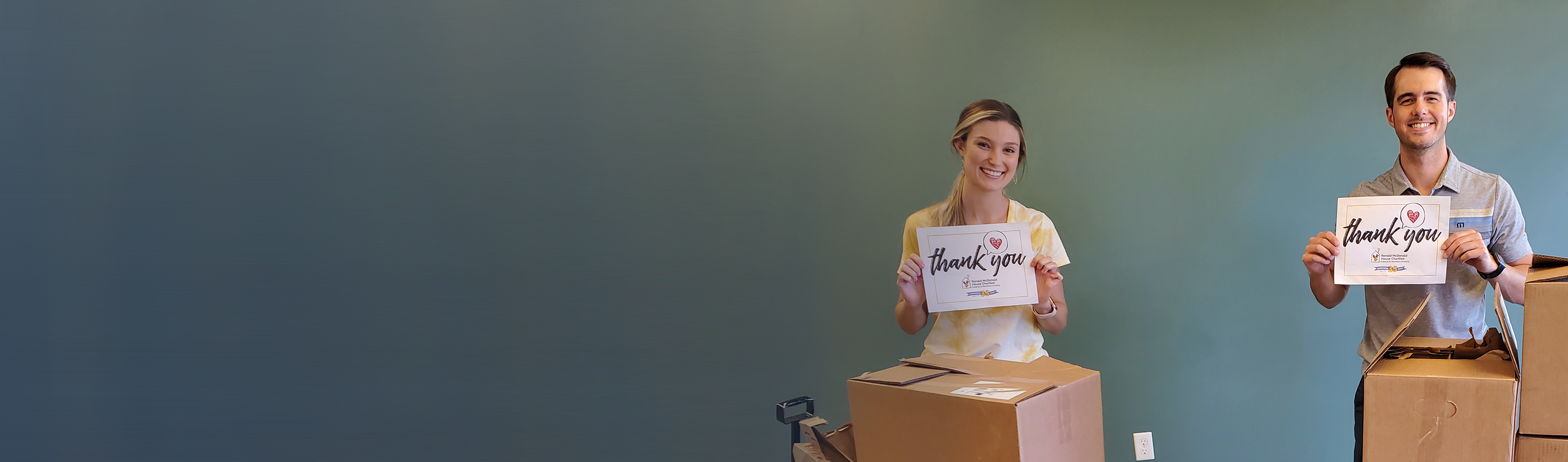 Two people standing behind brown boxes with thank you signs