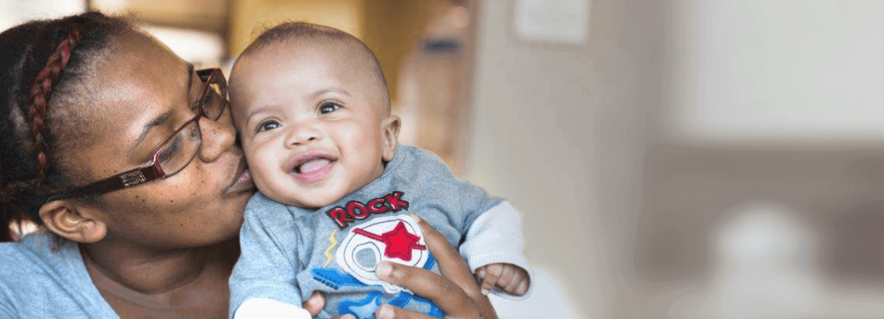 An RMHC family, mom holding up and kissing her smiling infant on the cheek