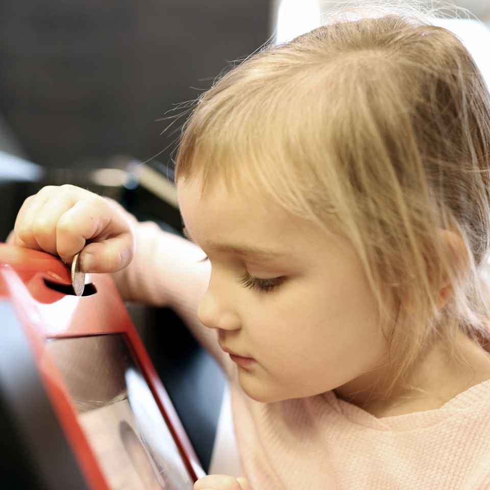 Close-up on a young child gazing through the donation box window as they drop a coin into it