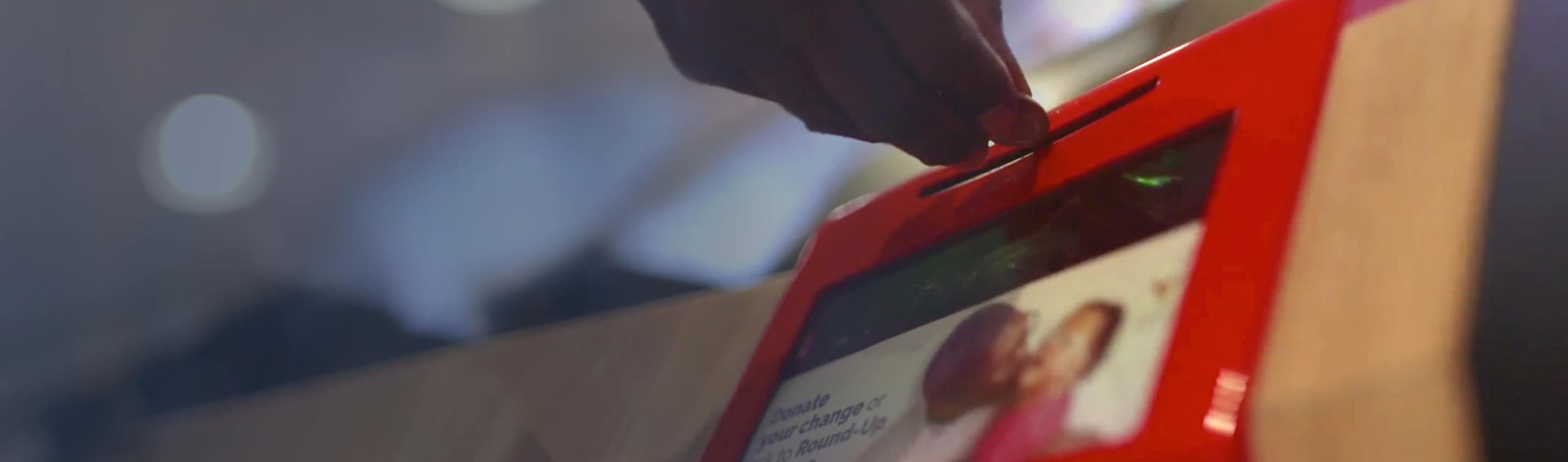 Close-up on an in-restaurant donation box, the hand of a McDonald's customer is placing spare change into the slot