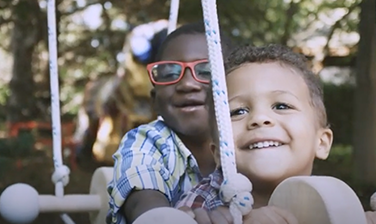 Daniel Jolivard, background, and younger brother Jacob playing, laughing on wooden swing