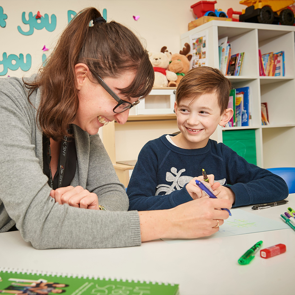 A volunteer and visiting child, holding pen and highlighter, sitting at a table reviewing a study sheet