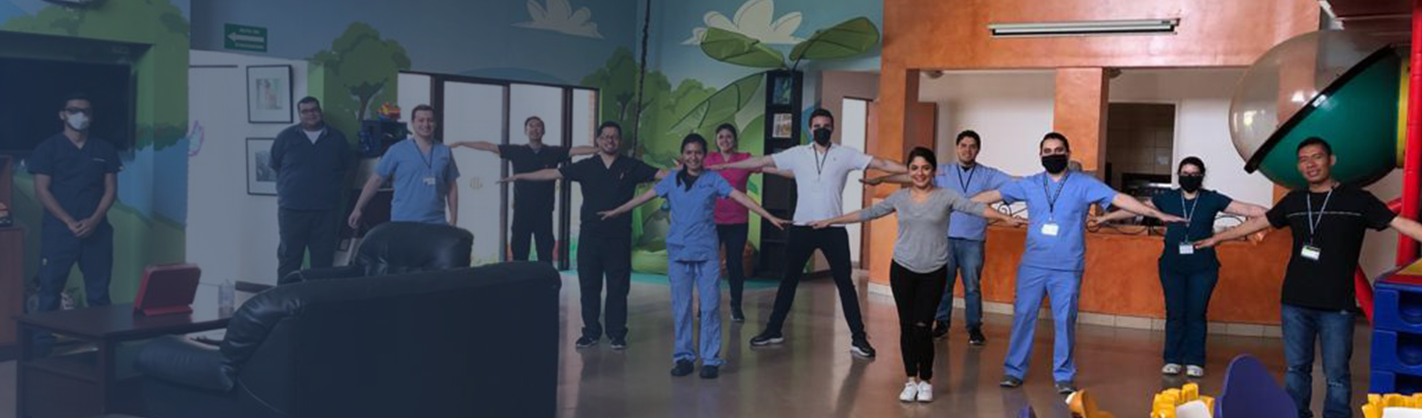 13 healthcare workers and administrators demonstrating social distancing, most wearing face masks and holding arms outstretched to show at least 6 feet of personal space