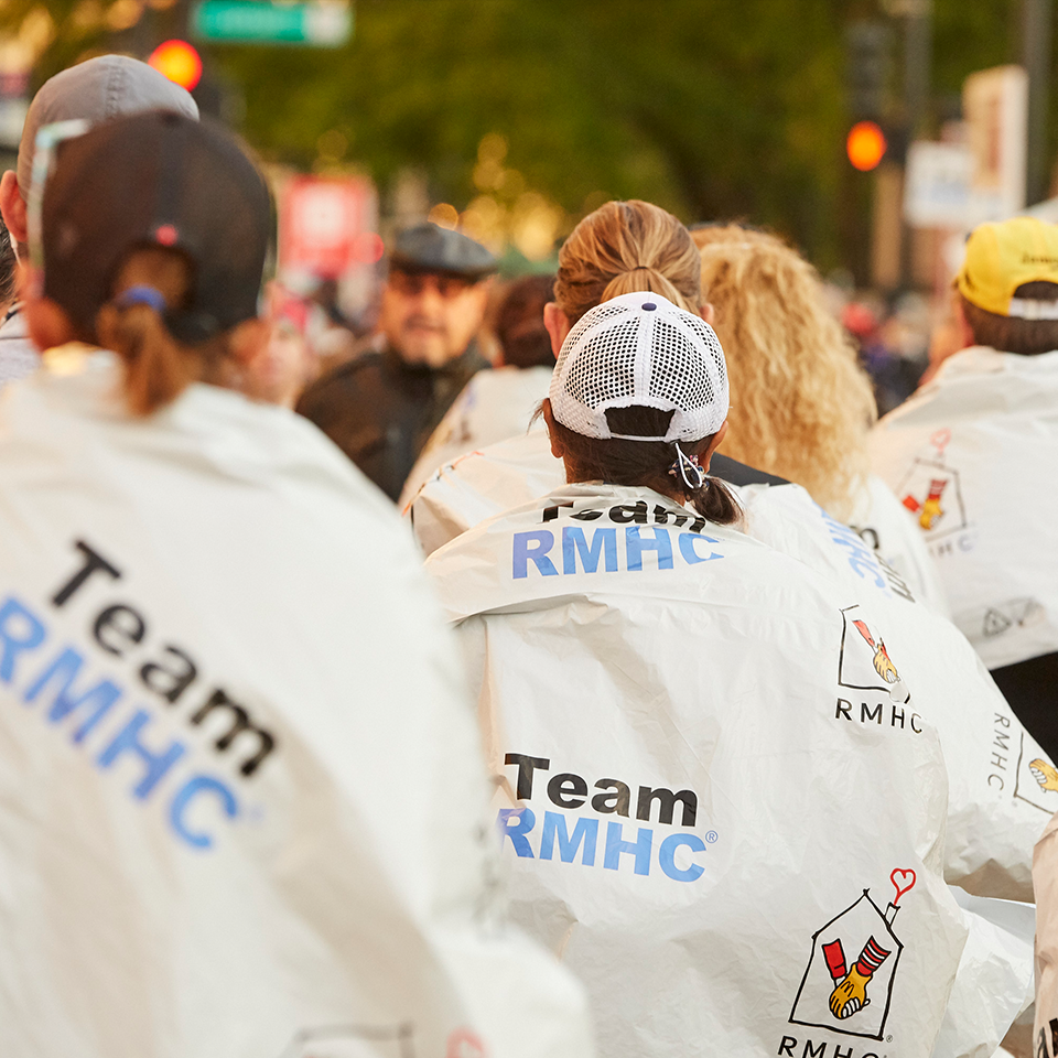 Team RMHC marathoners in baseball caps, turned away from camera, showing space blankets branded with "Team RMHC" and the RMHC logo