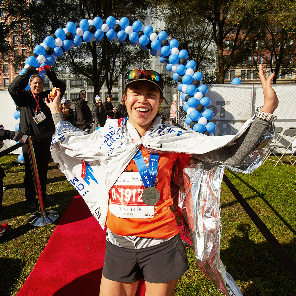 A Team RMHC marathoner after the finish line, wearing a baseball cap, space blanket, bib, and medal